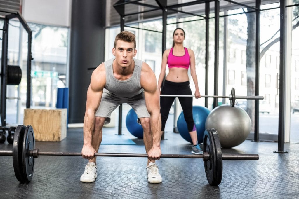 Fit couple lifting barbell at crossfit gym